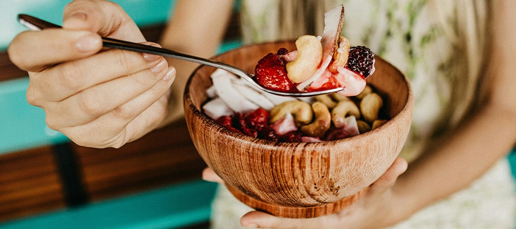 Person holding steel spoon with acai bowl with fruits