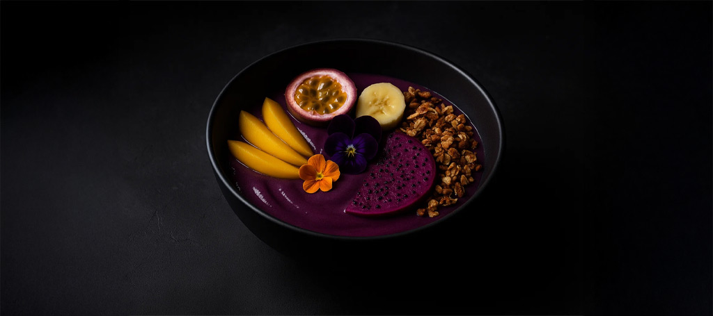 Amazon açaí TBS smoothie bowl with exotic fruits and edible flowers on a dark background, fine dining style.